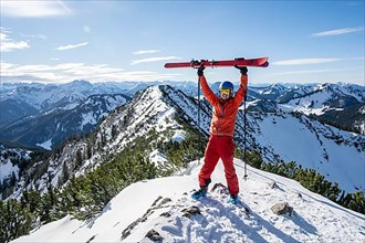 Ski tourer lifts his skis into the air at the summit of Jagerkamp, winter