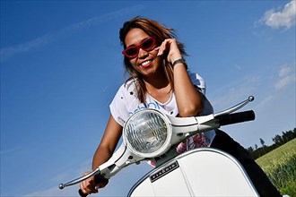 Woman with sunglasses sits on Vespa, rides on Vespa