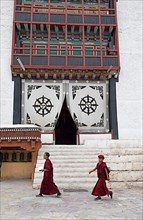 Two novices walk across the monastery courtyard, the entrance portal at the back