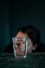 A woman's curious face reflected in a glass of water,