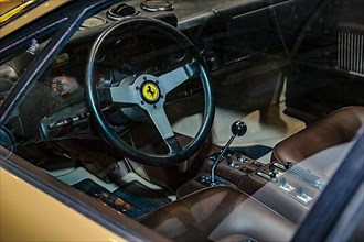 View into interior of Ferrari 512 BB from 70s 1977 with steering wheel with logo jumping horse Cavallino Rampante and lever of manual gear shift, fair Techno Classica