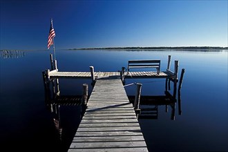 Early morning boat dock and star-spangled banner flag over calm reflection water on Lake of the Woods near Warroad Minnesota USA,
