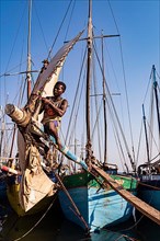 Man sitting on the yard of a fishing boat in the Arab quarter, repairing the square sail