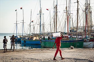 Man in red clothes carrying sack, fishing boats behind