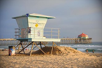 A lifeguard tower on a californian beach at sunset. Far behind is Huntington Beach Pier,