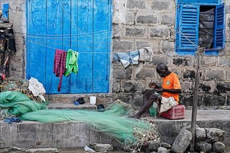 Man mending nets in front of his house, Elmina