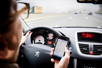 Female driver with mobile phone at the wheel, navigation