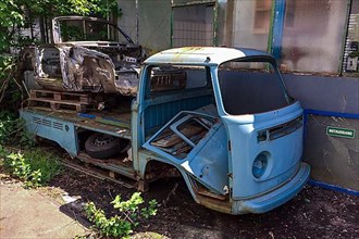 Rusty body from wreck of historic classic sports car classic car Porsche 911 lies on loading area of rusty wreck of VW Bulli t2 transporter lies in backyard, Germany