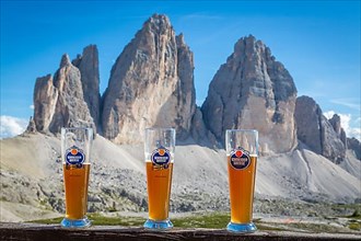 Three wheat beer glasses with wheat beer in front of the Drei Zinnen mountain range, north faces