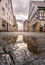 Paved street with puddle in the foreground and historic half-timbered houses