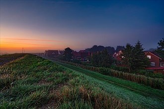 Sunrise behind the old dune with a view of the small village of Greetsiel under a cloudless sky