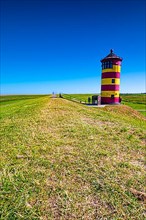 The Pilsum lighthouse on the dike in summer near Greetsiel on the North Sea