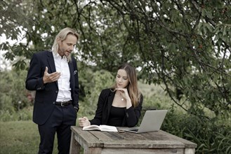 Businessman and businesswoman working in the open on a laptop at a wooden table