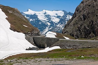 Bridge of mountain road in high Alps over glacier runoff of eternal snow melting in the background