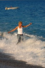 Young woman running in sleeveless white shirt and jeans on black beach of East Atlantic through surf waves spray