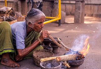 An old lady burning woods using a wind pipe at Kokkarebellur