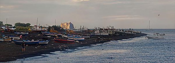 Boats on the sandy beach of San Vincenzo the volcano and Stromboli island at sunset