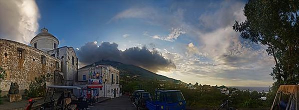 Village square with church Chiesa di San Vincenzo in front of the volcanic cone of Stromboli at sunset