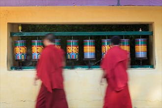 Buddhist monks passing and rotating prayer wheels on kora around Tsuglagkhang complex in McLeod Ganj