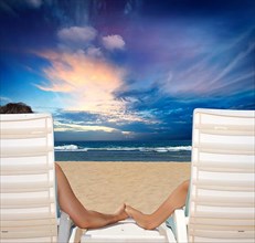 Couple in beach chairs holdi hands on beach and enjoy sunset