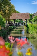 View of a covered wooden footbridge with flowers in the foreground
