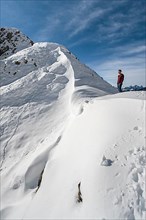 Hiker standing at a snow cornice at a saddle