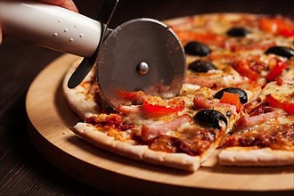 Pizza cutter wheel slicing ham pizza with