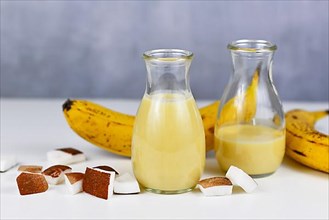 Helathy yellow banana and coconut smoothie drink in jars next to ingredients