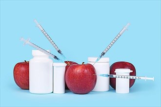 Apple fruits injected with syringes next to pill bottles. Concept for genetically modified food or pesticides