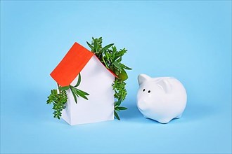 Concept for cost and energy efficiency and carbon neutrality in buildings by using green construction designs and renewable energy showing house with leaves and piggy bank