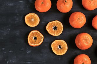 Slices of mandarins and whole fruits with peel on dark background