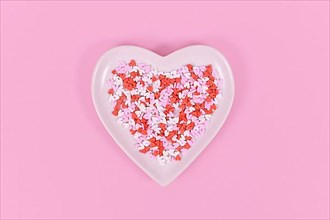 Plate with heart shaped sugar sprinkles on pink background