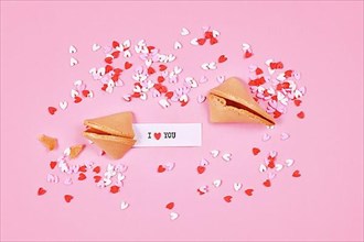 Fortune cookies with text 'I love you' and sugar sprinkle hearts on pink background