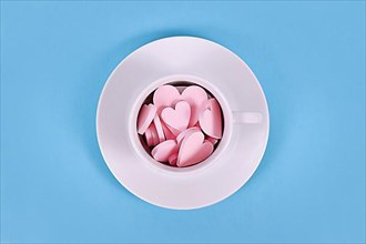 Pink wooden heart ornaments in white tea cup on blue background