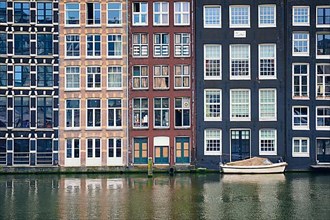 Row of typical houses and boat on Amsterdam canal Damrak with reflection. Amsterdam