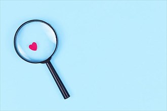 Looking for love concept with magnifier glass and pink heart icon on blue background with copy space