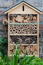 Insect hotel with artificial nesting facilities for solitary bees and burrows for hibernating ladybirds and butterflies near flower and vegetable garden