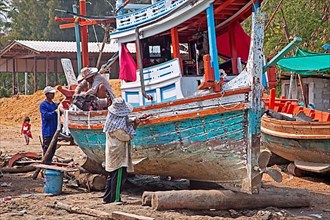 Boat builders renovating a traditional Thai wooden fishing boat on the beach in southern Thailand