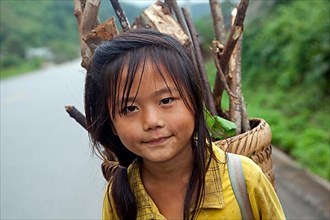 Close-up of a young Lao girl carrying firewood in a basket on her back