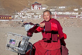 Young monk riding scooter in front of Sershu Dzong Tibetan monastery in Sershu village
