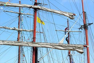 Two sailors climb the rigging to reach the yard of a sailing ship