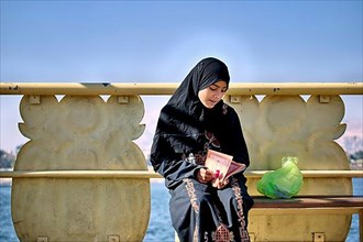 Young woman with headscarf reading on a Nile ferry. Luxor