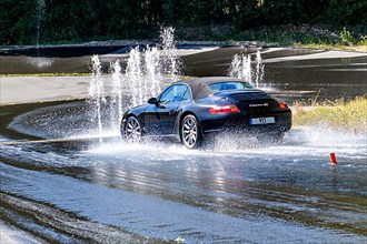 Sports car with all-wheel drive Porsche 911 Carrera 4s drives at 50 kmh speed on sloping heavily watered wet road towards obstacle from water fountain makes emergency stop avoids obstacles in curve