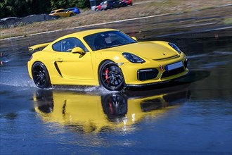 Sports car racing car Porsche Cayman GT4 on artificially rain wet road during driving safety training skids due to aquaplaning