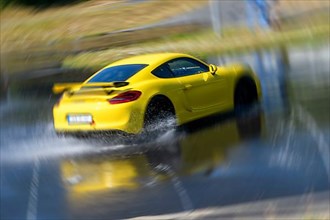 Sports car racing car Porsche Cayman GT4 on artificially rain wet road during driving safety training skids due to aquaplaning