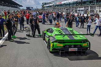 Motorsport fans audience of motor racing event inspects racing car Lamborghini Huracan GT3 on start-finish straight Gridlane of race track in front of start