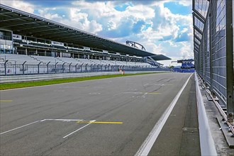 View through security fence from pit lane to empty start-finish straight grid lane with markings for start position