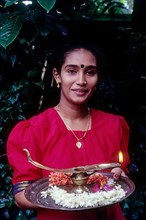 A girl holding oil lamp and flowers on a tray during Onam festival