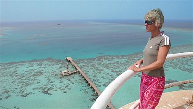 Woman looking at red sea reef with jetty from Sanganeb lighthouse