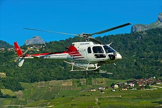 Helicopter Eurocopter AS350 B2 Ecureuil of Air-Glaciers SA flying over the wine growing area of Leytron at the foot of the Swiss Alps